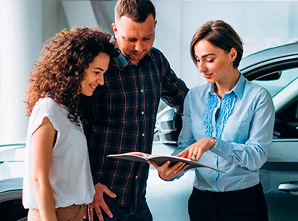 Two buyers going through a folder with an advisor beside a car