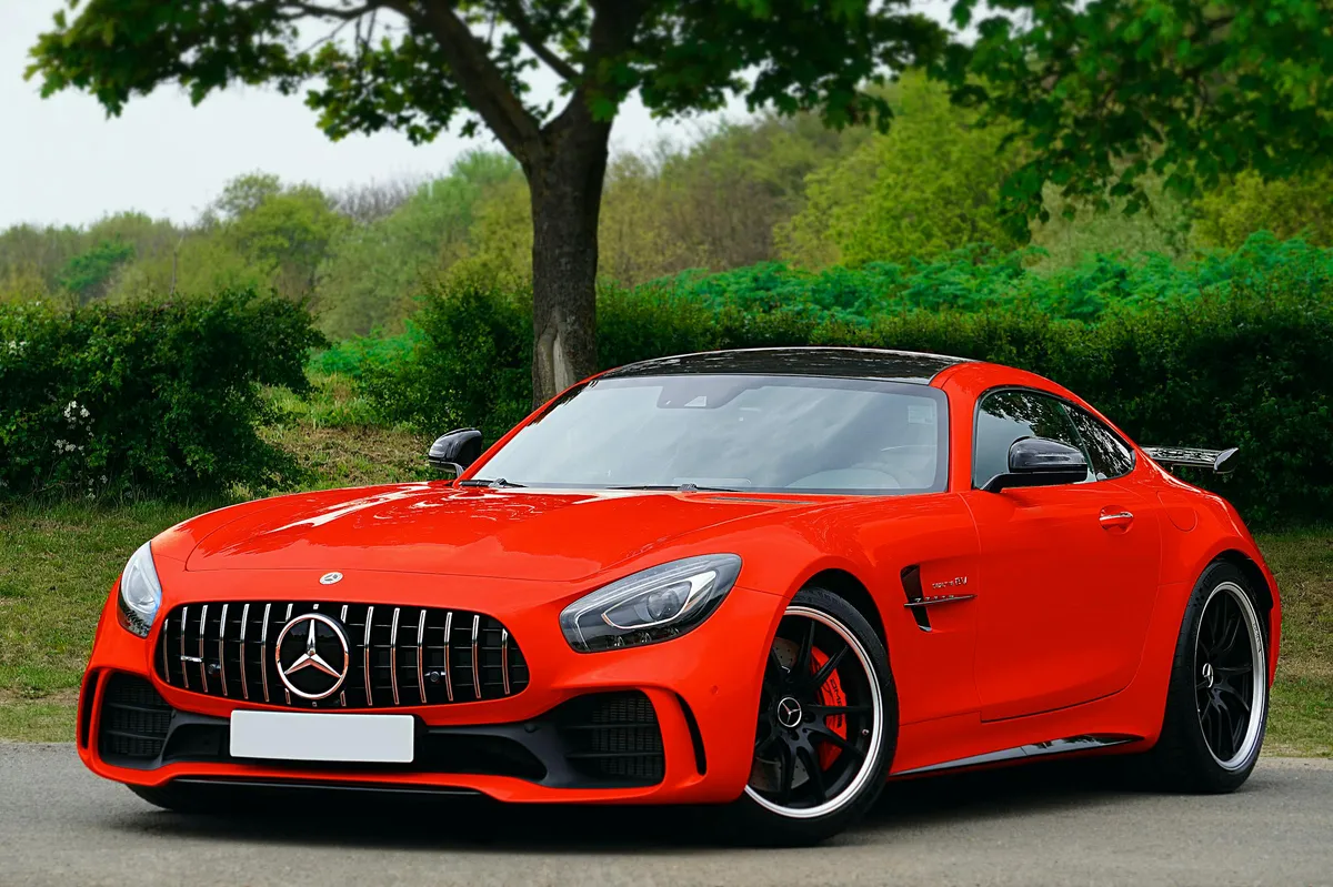 A red coupe parked on grass under a tree